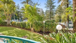 A lush garden with various tropical plants and a metal railing. - Aruba Beach - Private Apartments (Broadbeach)