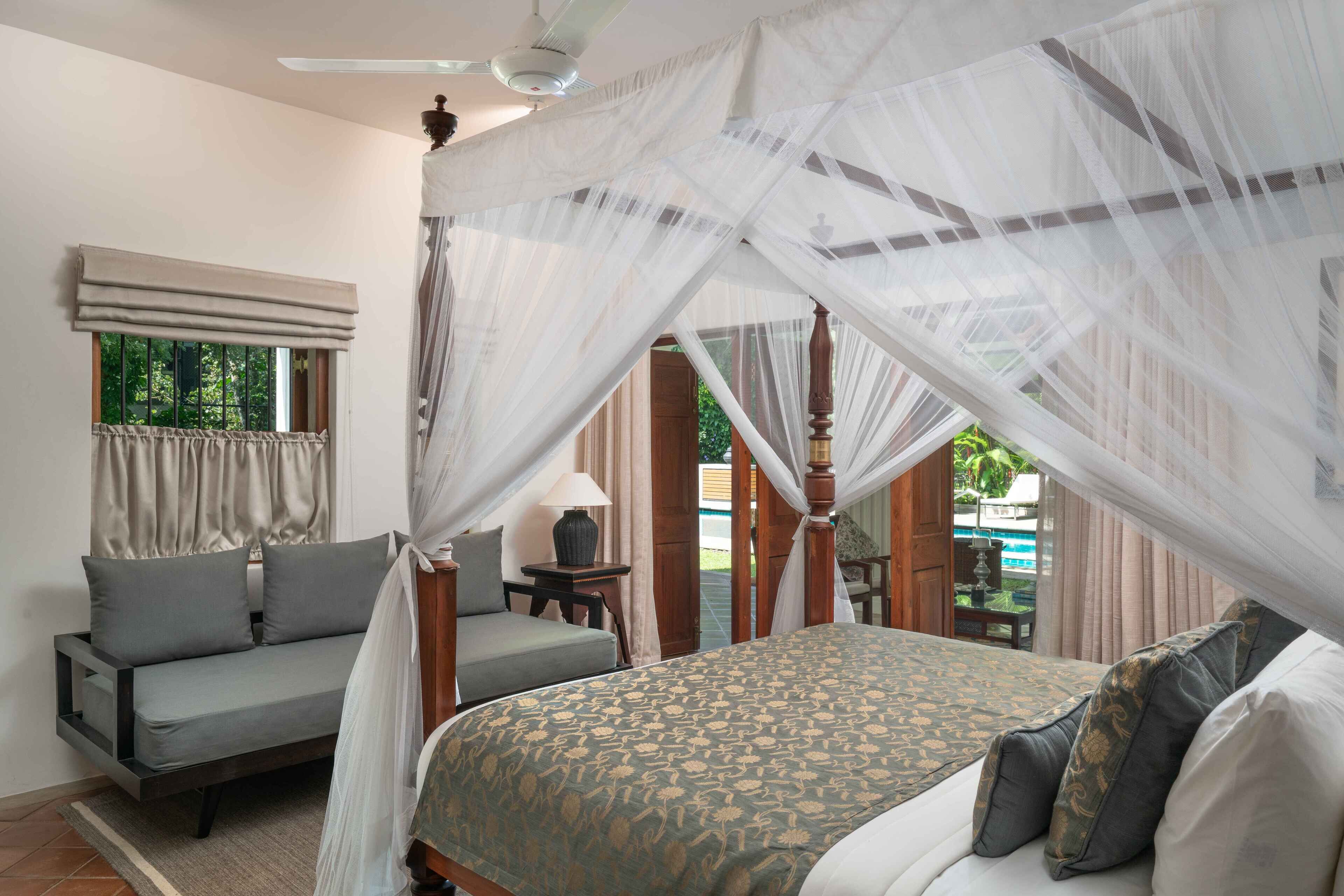 A bedroom with a canopy bed, a sofa, and a view of the outdoors.