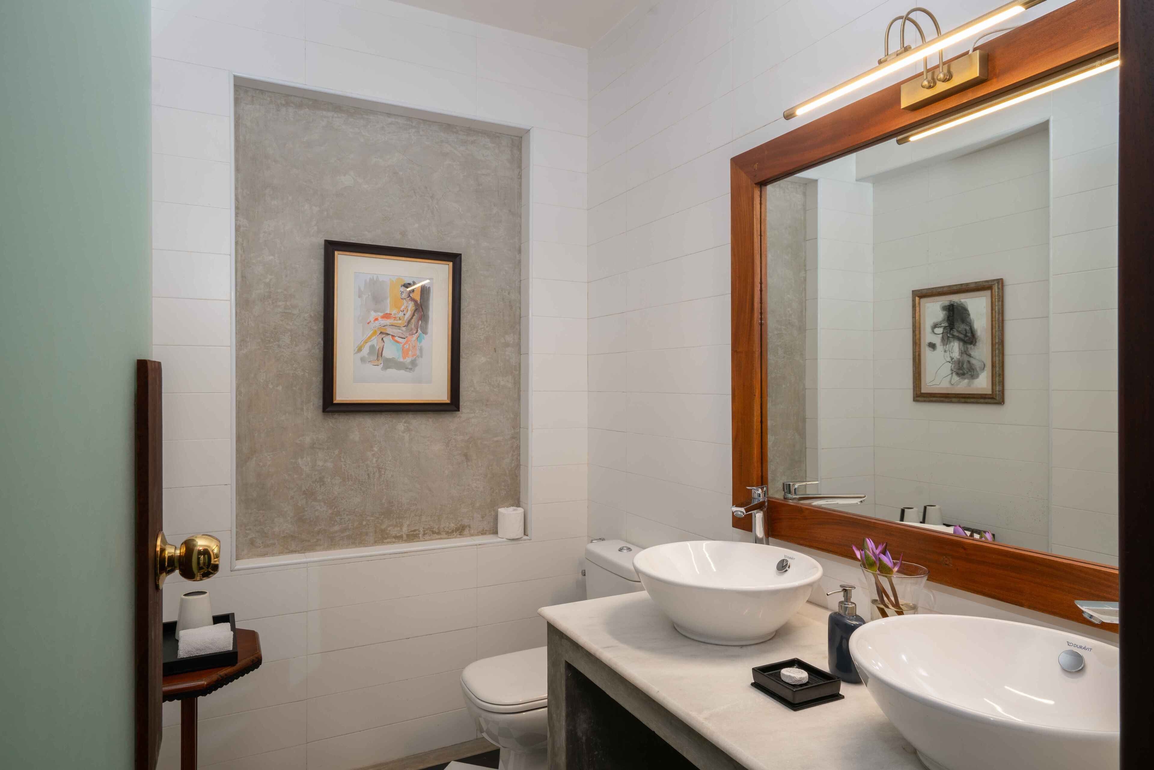 A modern bathroom with two sinks, a toilet, and a framed artwork on the wall.
