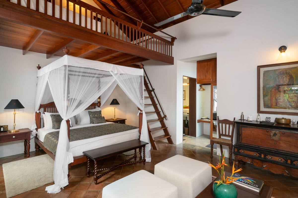 A bedroom with a four-poster bed, wooden staircase, and a desk with a chair.