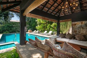 A covered outdoor area with a pool, lounge chairs, and a stone wall. - Taru Villas Kandy (Kandy)