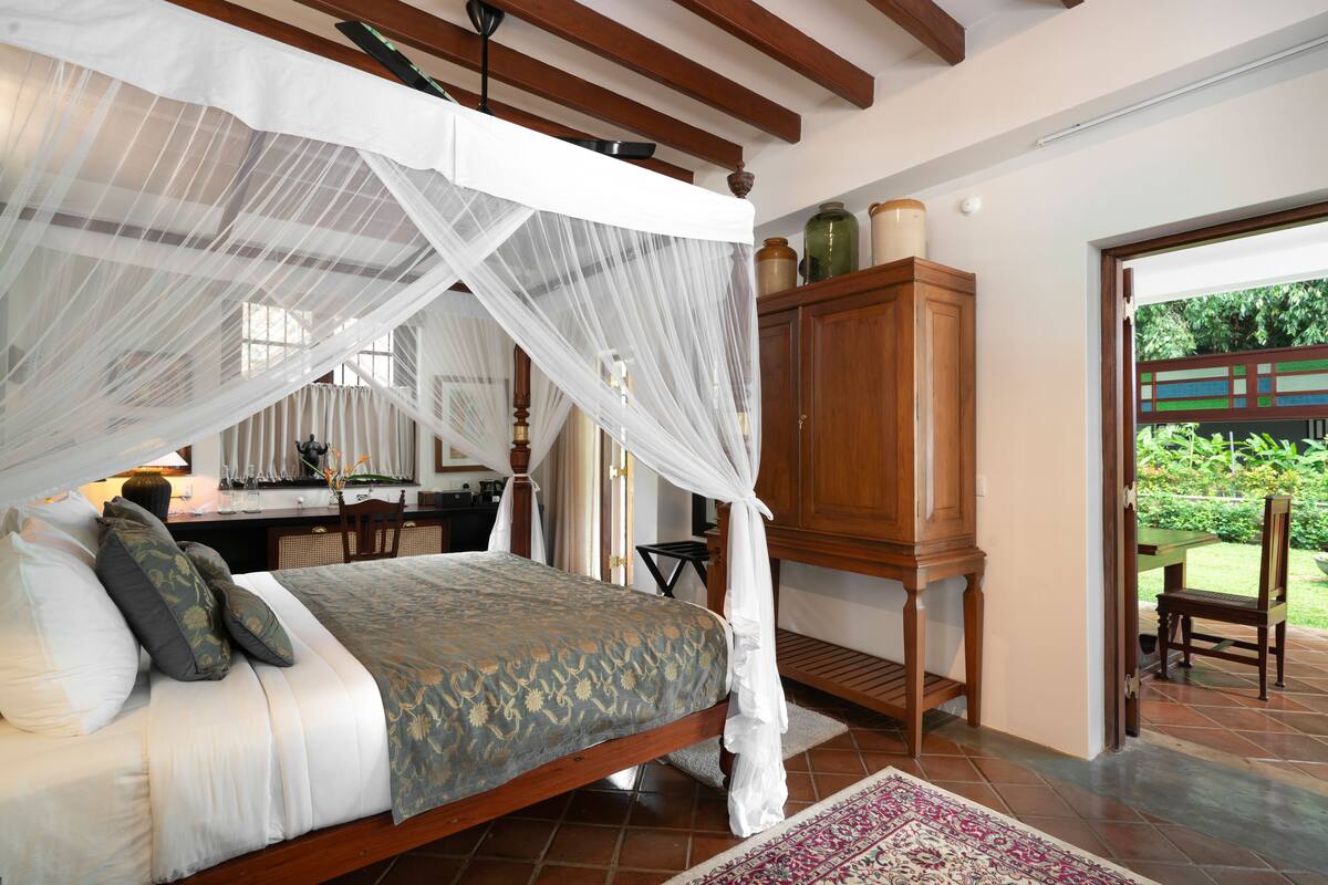 A bedroom with a canopy bed, wooden furniture, and a view of the garden.