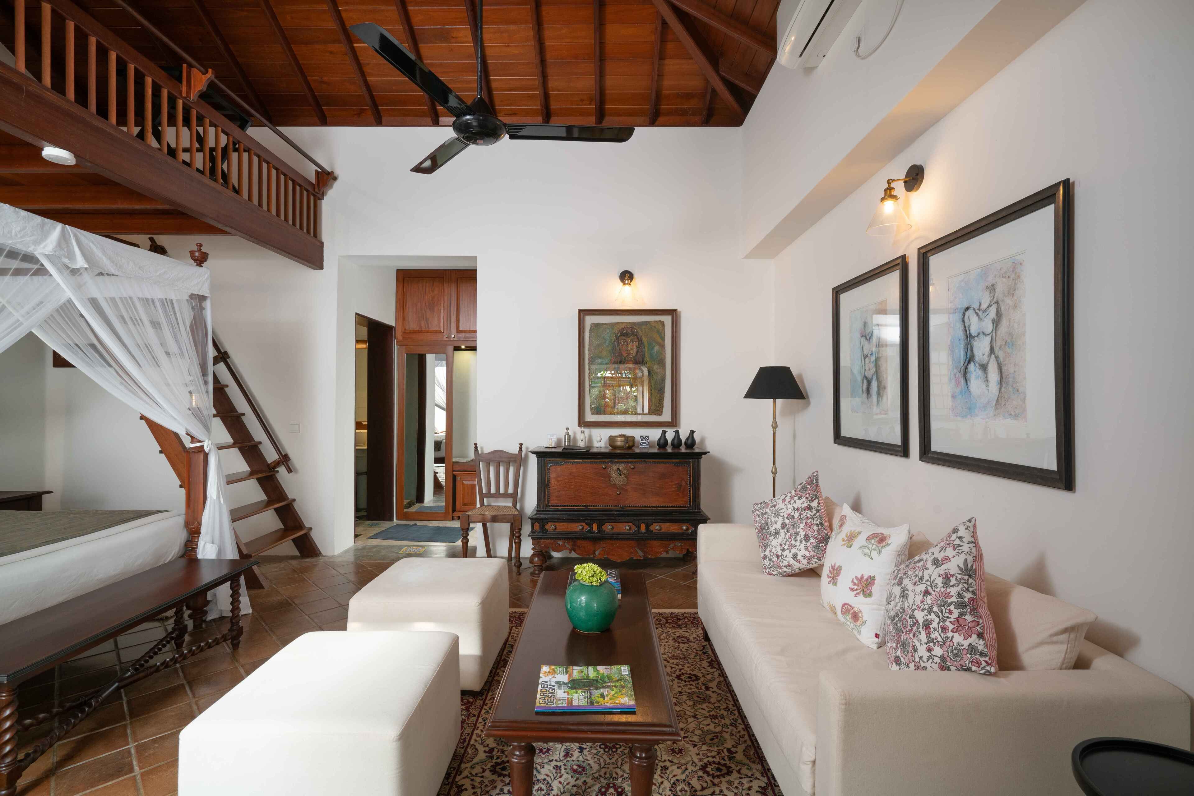 A spacious living room with a high ceiling, a wooden staircase, a sofa set, a coffee table, and a decorative vase.