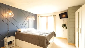 A bedroom with a bed, bedside tables, a TV, and a window.