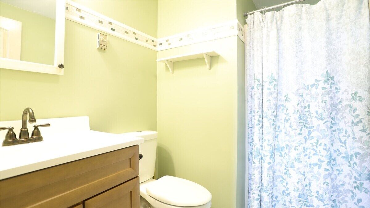 A bathroom with a white sink, a mirror, a toilet, and a shower curtain.