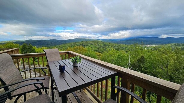 Eine Holzterrasse mit Sitzgelegenheiten und einem Tisch, mit Blick auf eine bewaldete Landschaft.