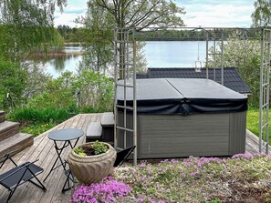 A covered outdoor seating area with a table and chairs, a hot tub, and a garden with pink flowers.