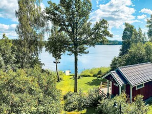A lakeside cabin with a deck, surrounded by dense trees and a clear view of the lake.