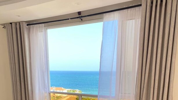 A hotel room with a large window offering a view of the sea and a distant landscape.