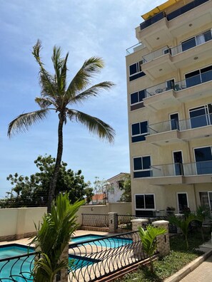A multi-story building with balconies, a swimming pool, and palm trees. - Nyali Mall Apartments by CHH (Mombasa)