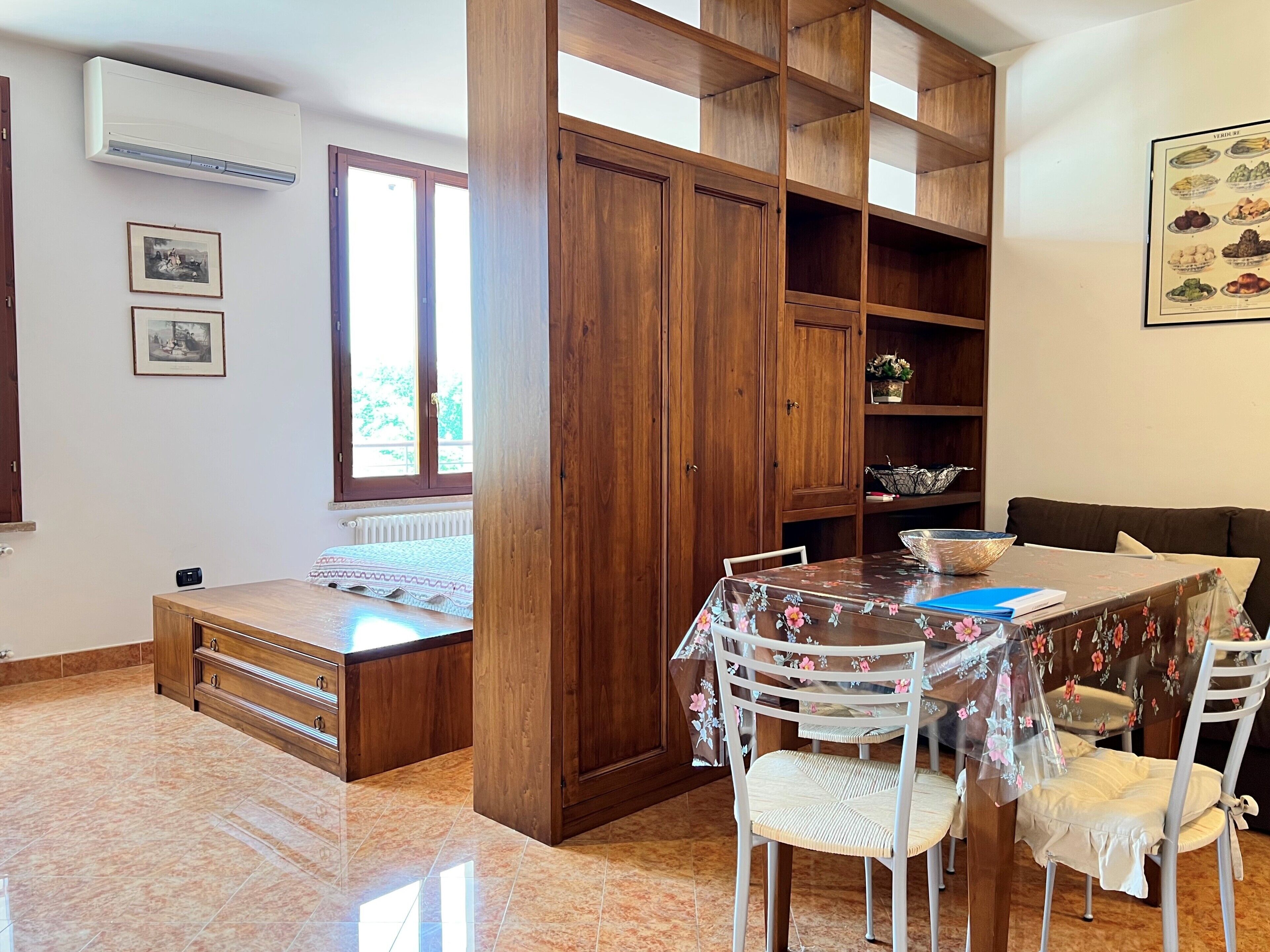 Quarto com armário de madeira, mesa de jantar com cadeiras, radiador e um quadro na parede.