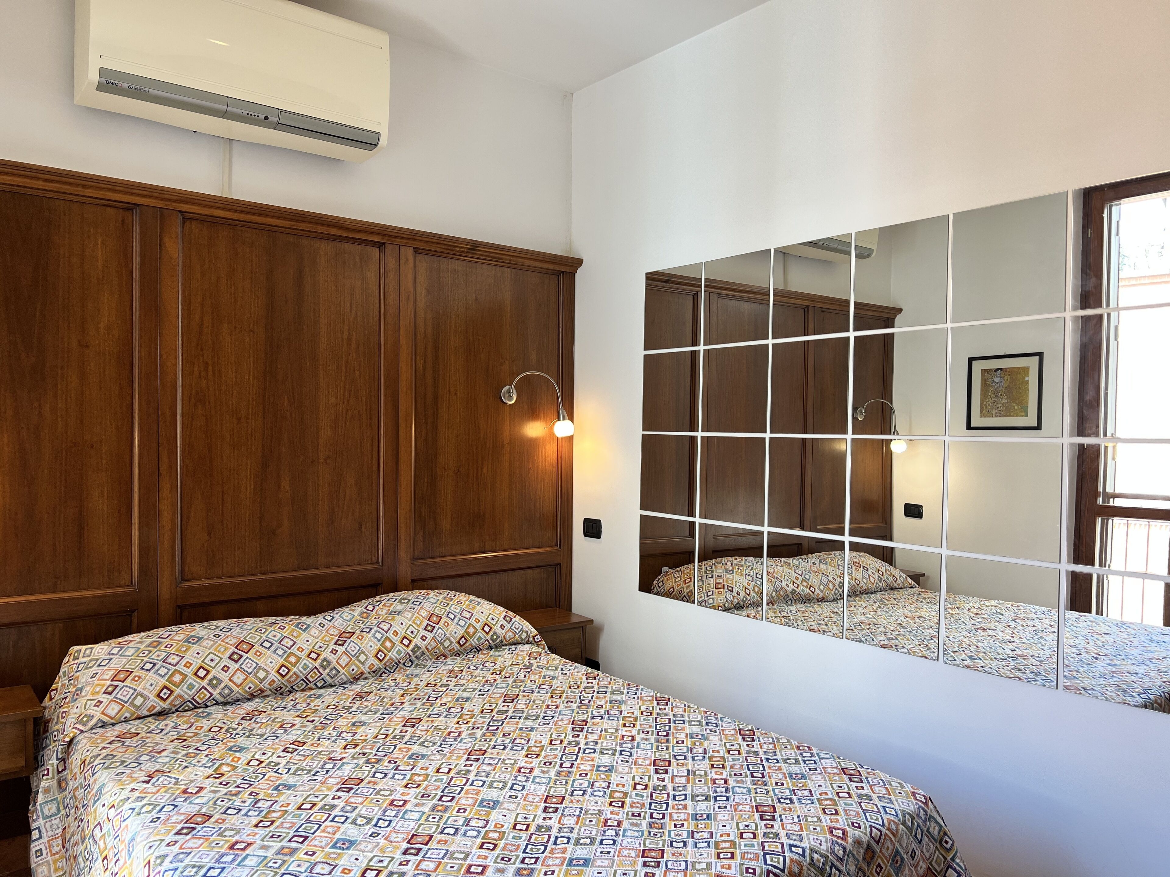 Een slaapkamer met een grote spiegel, een houten kledingkast en beddengoed met een patroon.