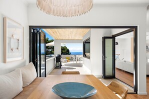 Um interior moderno com uma mesa de jantar de madeira, uma tigela azul e vista para uma varanda com móveis de exterior.