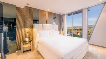 A modern hotel room with a large bed, a bedside telephone, and a city view through large windows.