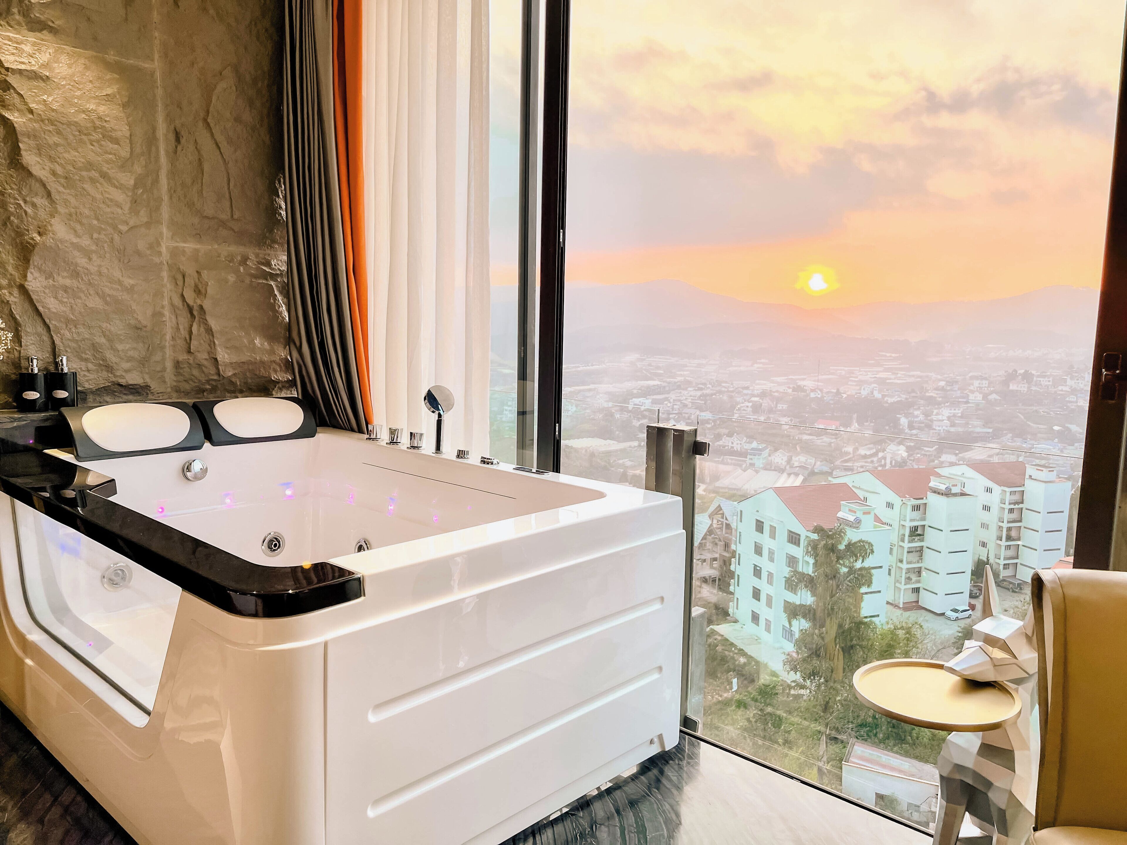 Een moderne badkamer met een groot bad, een douchecabine van glas en een uitzicht op een stadsbeeld bij zonsondergang.
