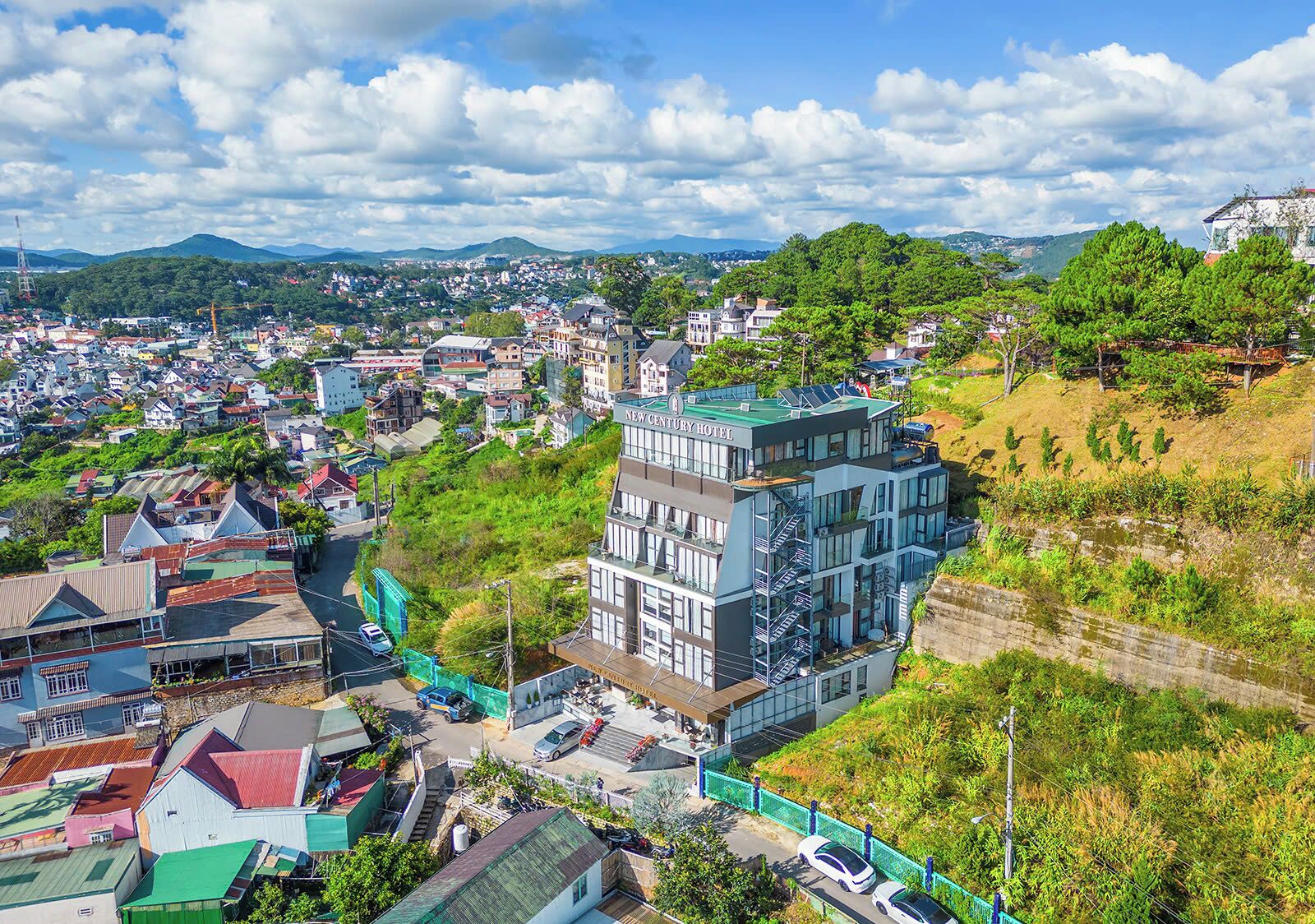 A modern hotel with a green roof, surrounded by a residential area with various buildings and greenery.