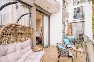 Un balcón con mobiliario de mimbre, una mesa de vidrio y vista al interior del edificio.
