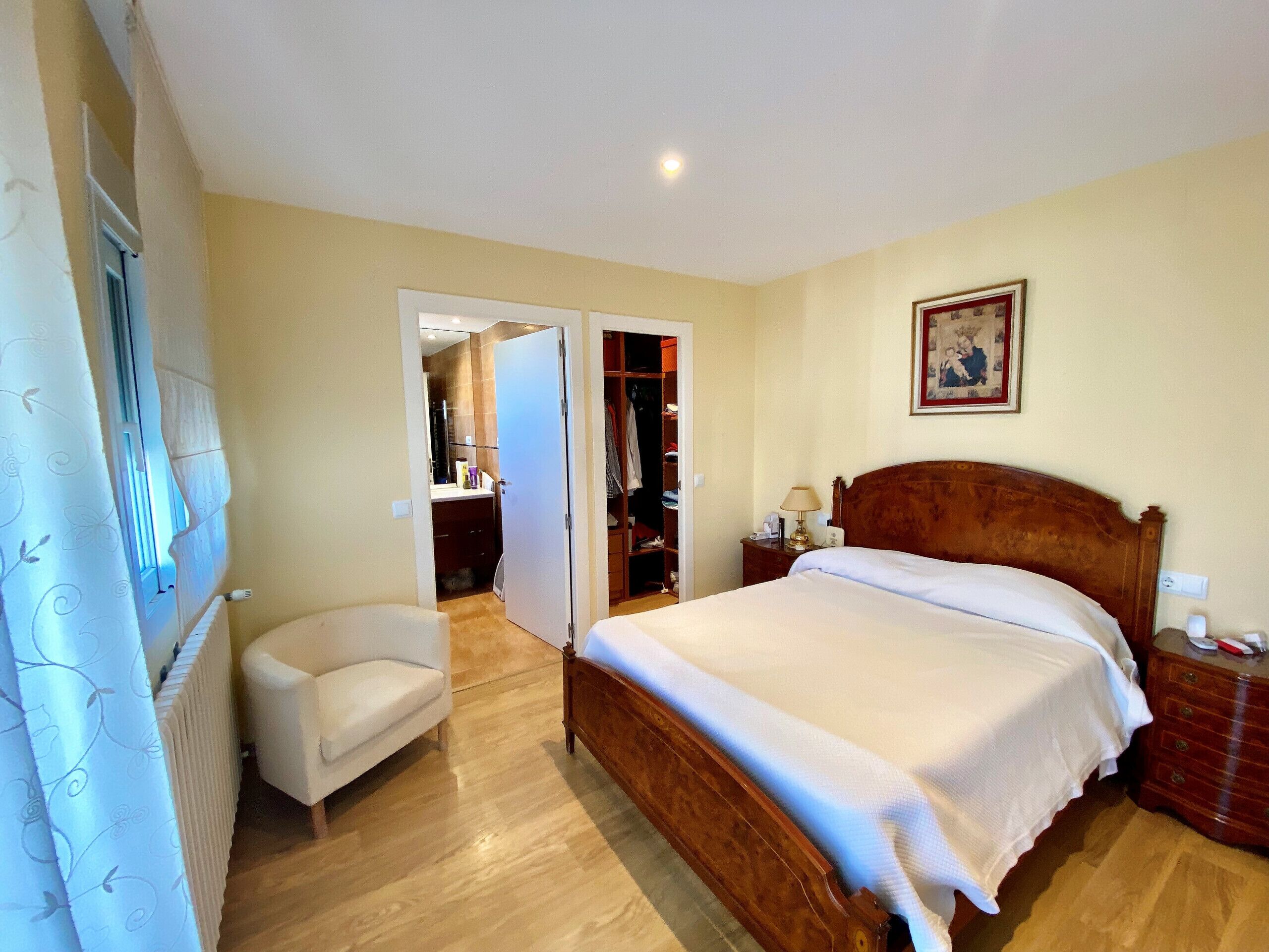 A bedroom with a wooden bed, a bedside table with a lamp, a chair, and a wardrobe.
