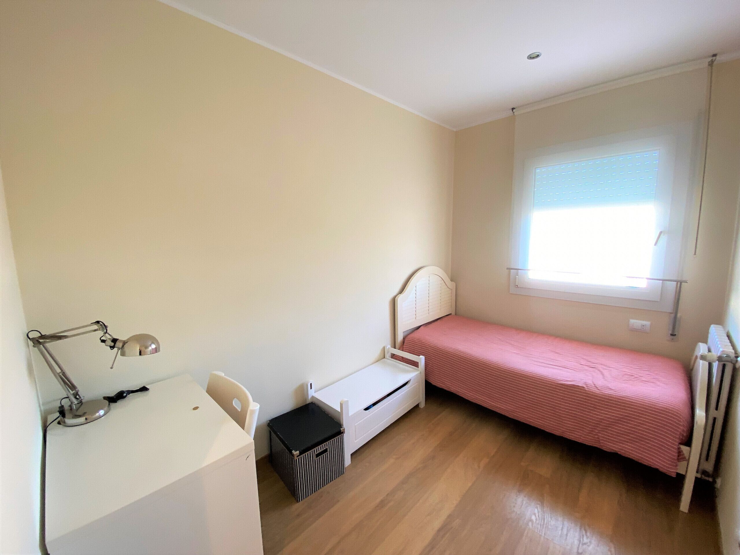 A small, single-bed room with a desk, chair, and a radiator.
