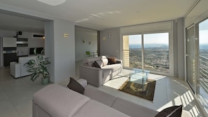 Una sala moderna con un sofá, una mesa de centro y vistas de la ciudad a través de amplios ventanales.