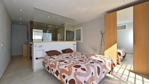 Un dormitorio moderno con una cama grande, un armario empotrado y un espejo amplio.