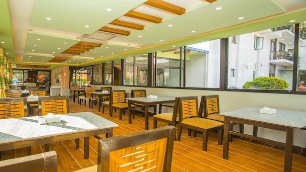 Un restaurant avec des tables et des chaises en bois, de grandes fenêtres et un mur en briques.
