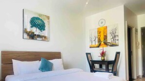 Une chambre d’hôtel avec un grand lit, une tête de lit en bois, une petite table sur laquelle est posé un vase de fleurs, et deux tableaux accrochés au mur.