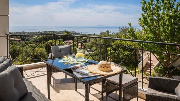 Ein Balkon mit Korbmöbeln, einem Tisch mit Getränken und Blick aufs Meer.