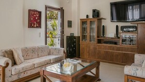 Ein Wohnzimmer mit einer Couch, einem Glastisch, einem Holzschrank und einem Fernseher.
