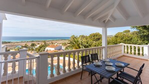 A covered outdoor area with a table set for dining, a pool, and a view of the sea and landscape. - Villa '49 Son Bou Sunset' with Sea View, Wi-Fi and Air Conditioning (MENORCA)