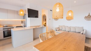 A modern kitchen with a central island, a dining area with a wooden table, and wicker chairs. - Villa '49 Son Bou Sunset' with Sea View, Wi-Fi and Air Conditioning (MENORCA)
