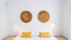 A bed with white bedding and two yellow pillows, a wooden nightstand, and two wall-mounted woven wall art pieces. - Villa '49 Son Bou Sunset' with Sea View, Wi-Fi and Air Conditioning (MENORCA)