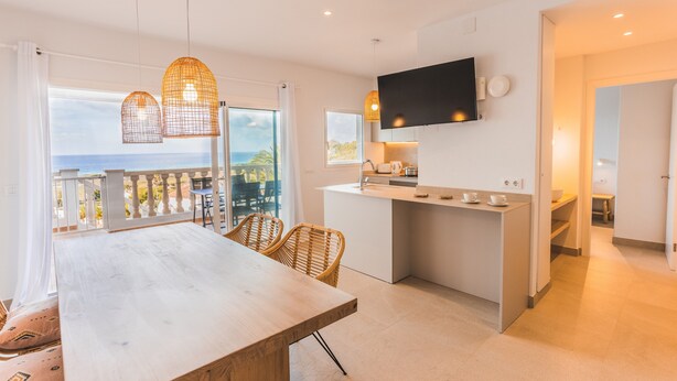 A modern kitchen with a TV, dining area with chairs, and a balcony with a view. - Villa '49 Son Bou Sunset' with Sea View, Wi-Fi and Air Conditioning (MENORCA)