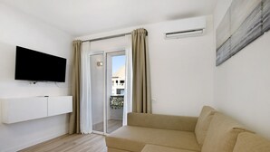 Un salón moderno con un televisor de pantalla plana, un sofá, un ventanal corredero y vistas a un edificio.