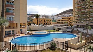 Una piscina rodeada de una valla, con vistas a edificios residenciales al fondo.