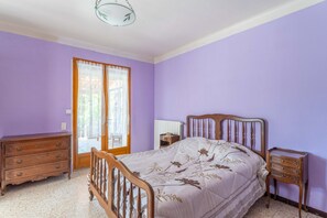 A bedroom with a bed, wooden dresser, nightstand, and a window with curtains.