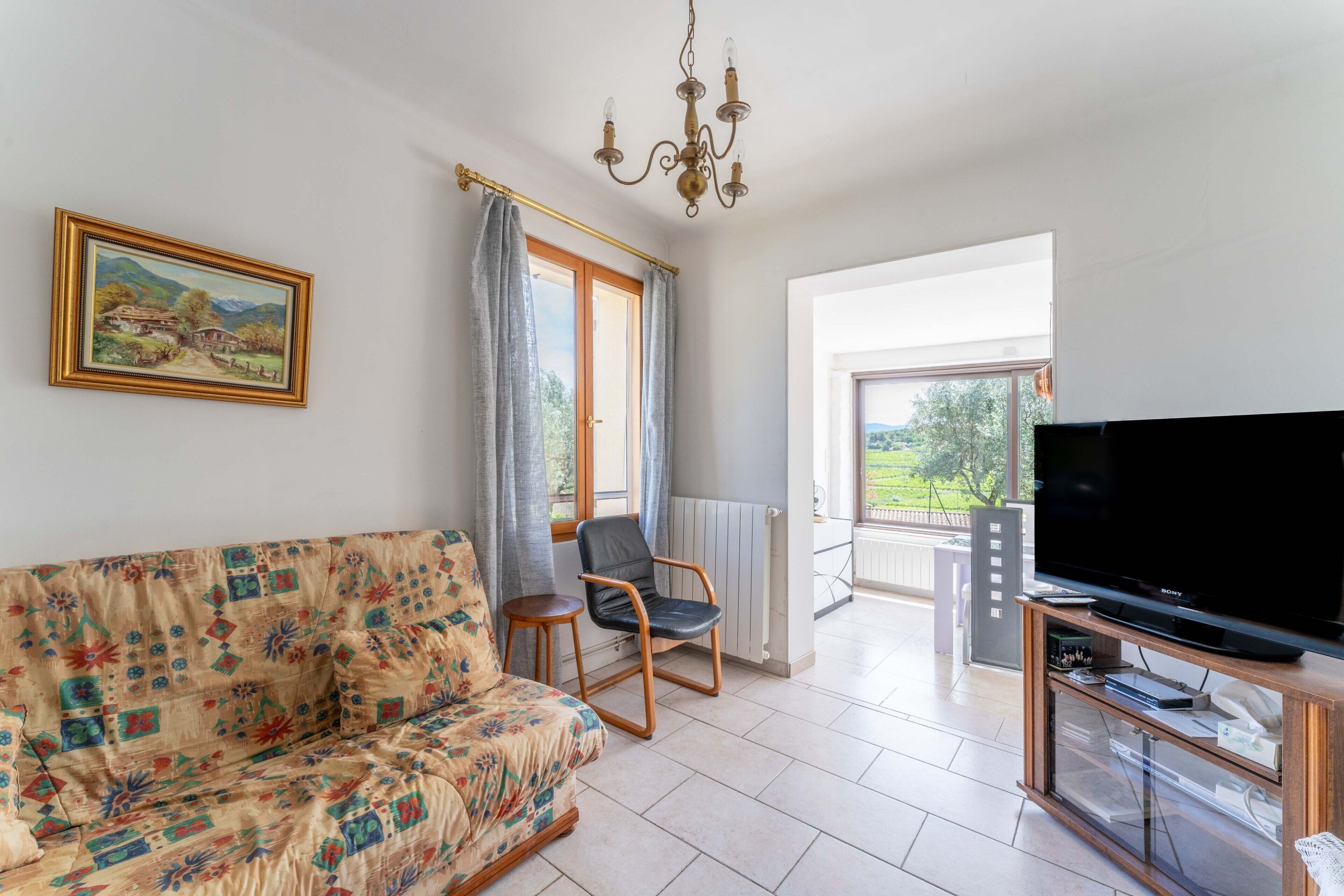 Ein Wohnzimmer mit einer Couch, einem Sessel, einem Fernseher und einem Gemälde an der Wand.