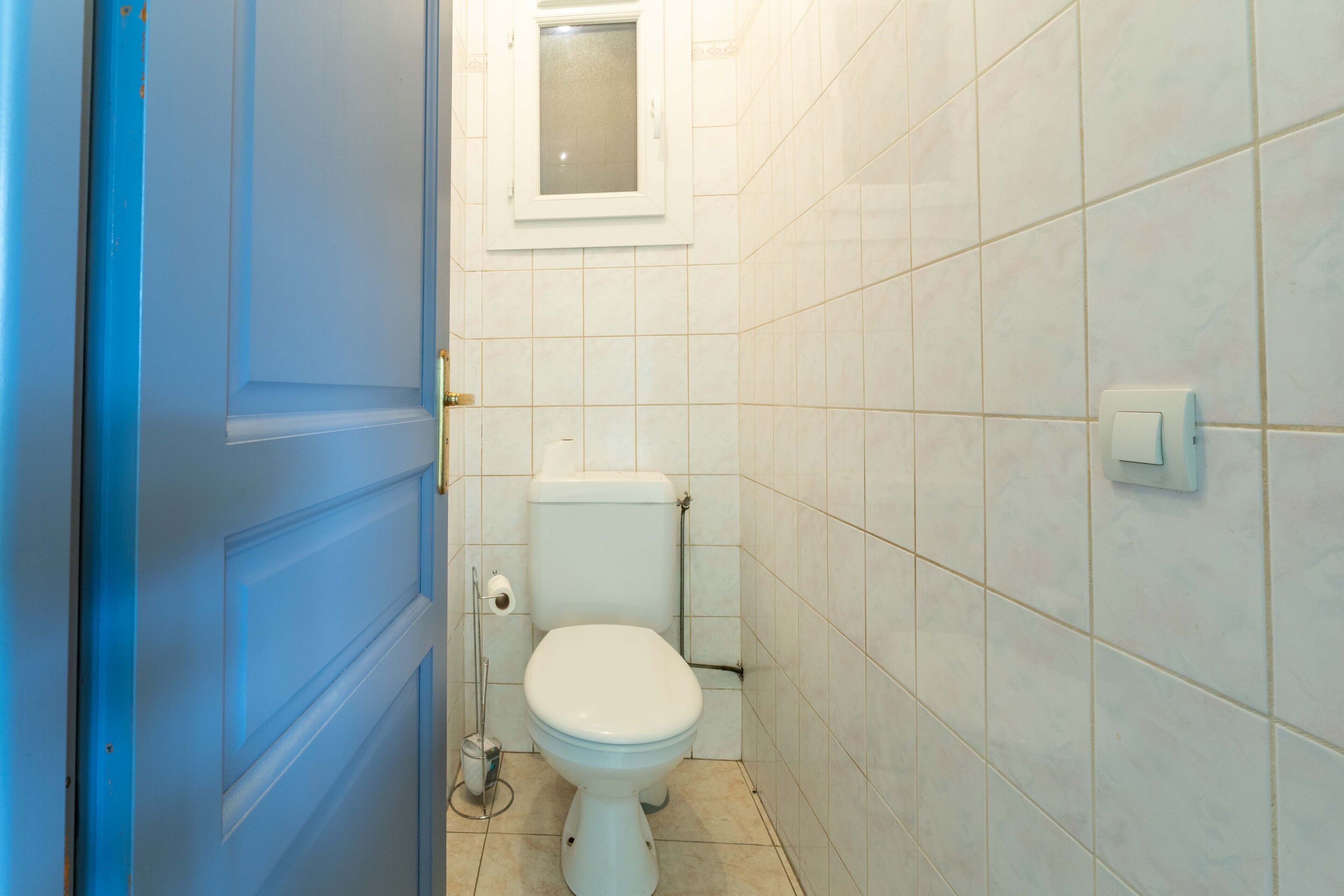 A small bathroom with a toilet, a window, and a door.