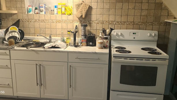 A kitchen with white cabinets, a stove, and various kitchen items on the counter.