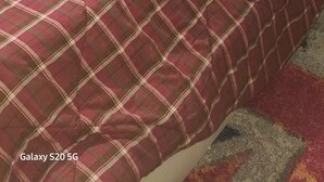 A bed with a plaid bedspread, a remote control, and a patterned pillow on a small table beside it.