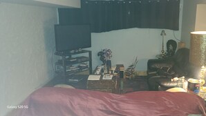 A bedroom with a bed, a television, a lamp, and a small table with various items.