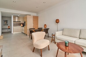 Una sala de estar moderna con un sofá, una mesa redonda, un sillón mullido y un comedor con mesa y sillas.