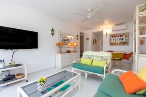 Un salon équipé d’un téléviseur à écran plat, d’un ventilateur de plafond, d’un canapé avec des coussins, d’une table basse et d’un coin repas comprenant une chaise et une table.