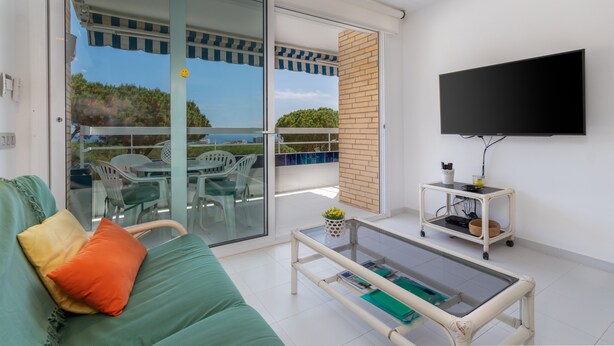 A modern living room with a sofa, a coffee table, a TV, and a balcony with outdoor furniture. - Apartment 'Les Magnolies' with Sea Views, Wi-Fi and Air Conditioning (PLAYA  DE  ARO)