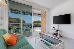 Una sala de estar moderna con un sofá, una mesa de centro, un televisor y un balcón con mobiliario exterior.