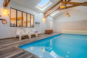 Une piscine intérieure dotée d’une terrasse en bois, d’un plafond en verre et offrant une vue sur un mur en pierre.