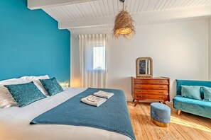 A bedroom with a bed, a dresser, a sofa, and a hanging light fixture.