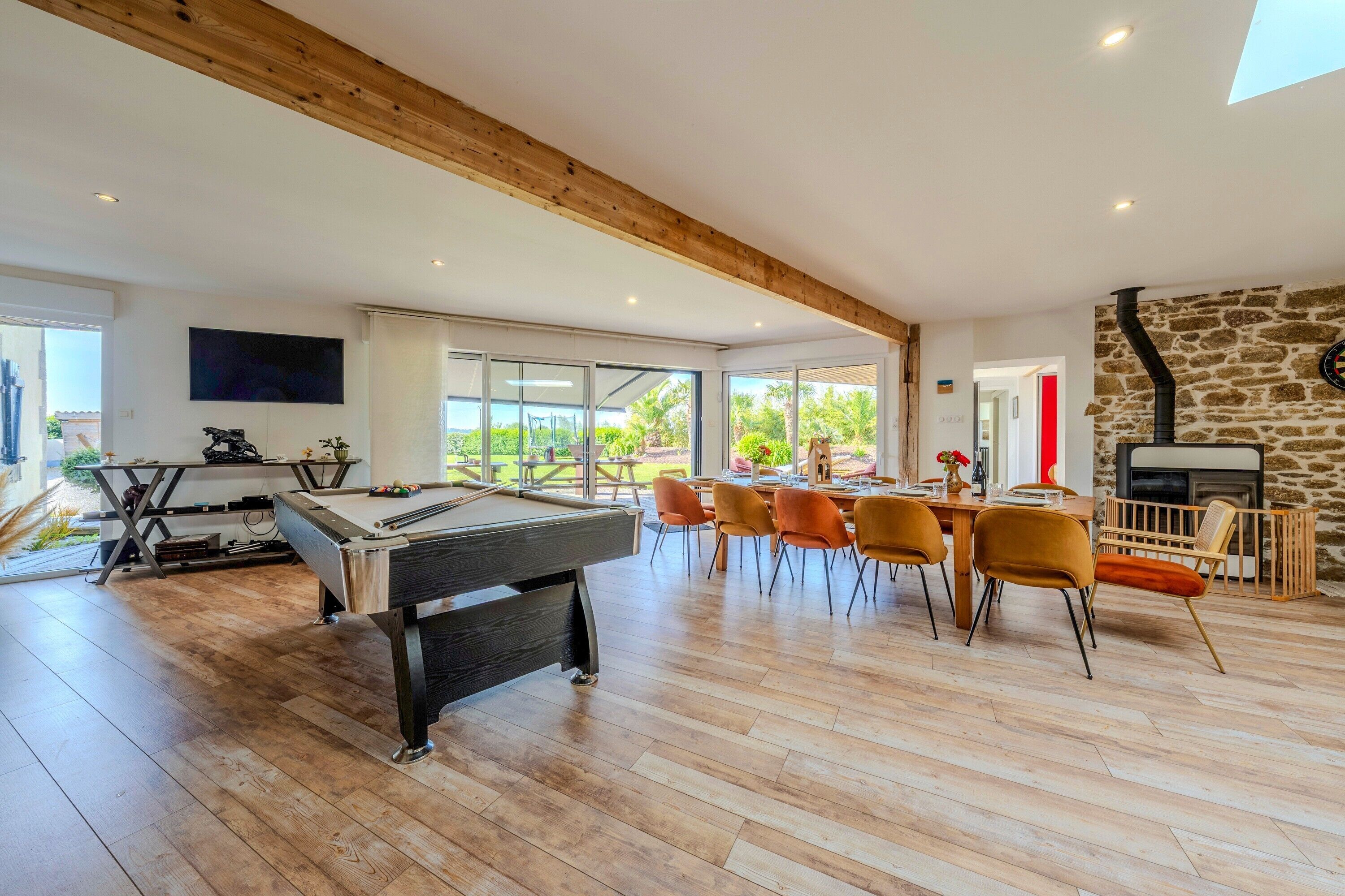 A spacious room with a pool table, dining area, and a stone fireplace.