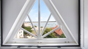 A triangular skylight window with a view of a beach and buildings. - Apartment 'Vista Baia' with Sea View, Shared Pool and Wi-Fi (São Martinho do Porto)