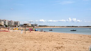 A beach with sand, water, and buildings in the background. - Apartment 'Vista Baia' with Sea View, Shared Pool and Wi-Fi (São Martinho do Porto)